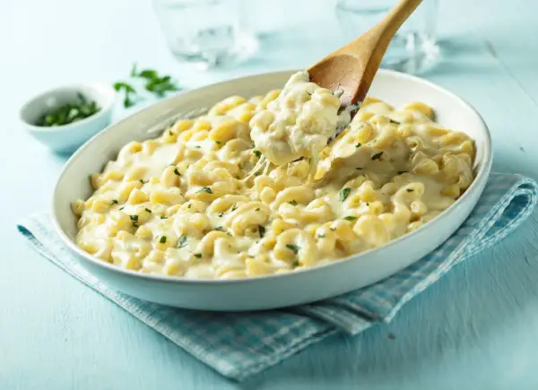 Pyszne mac and cheese przepis w białej misce, z drewnianą łyżką nabierającą porcję kremowego makaronu z serem.
