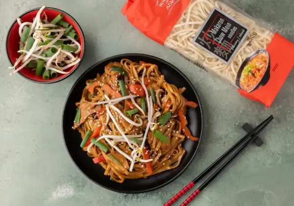 Gotowy do jedzenia makaron chow mein z warzywami i kiełkami fasoli. Obok opakowanie makaronu.